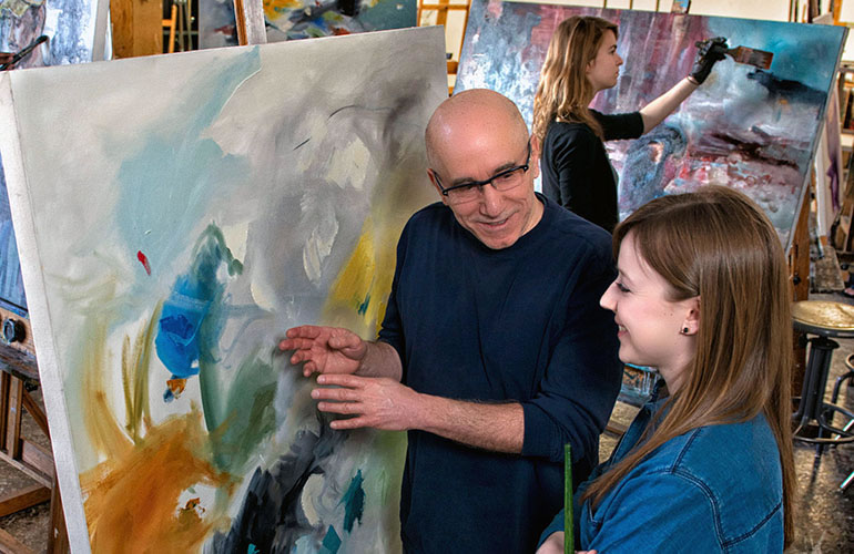 Professor and student in a painting studio looking a a canvas.